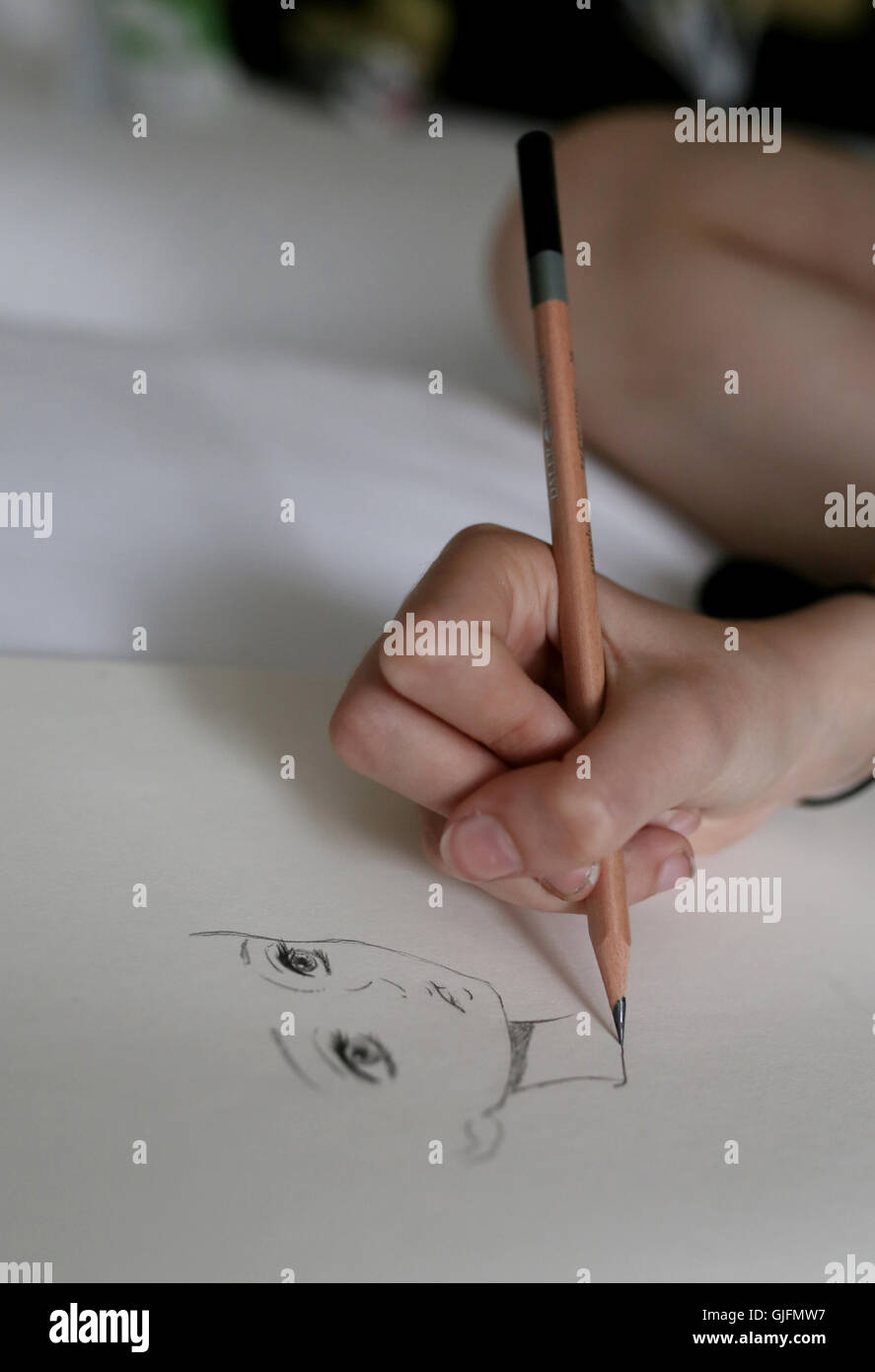 A girls hand holding a pencil and drawing a face, Manga style on white paper. Stock Photo