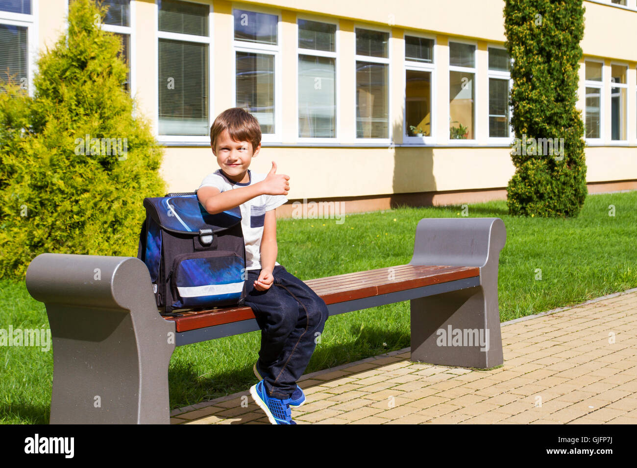 Little boy near preschool sitting on the bench. Child smiling. He