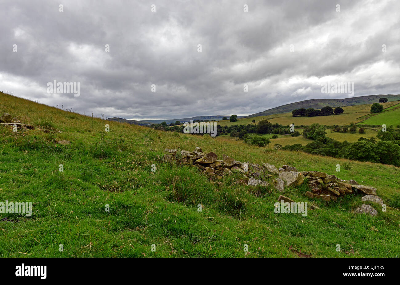 A crumbling dry stone wall in the Peak District National Park with rolling hills in the background under a grey cloudy sky Stock Photo