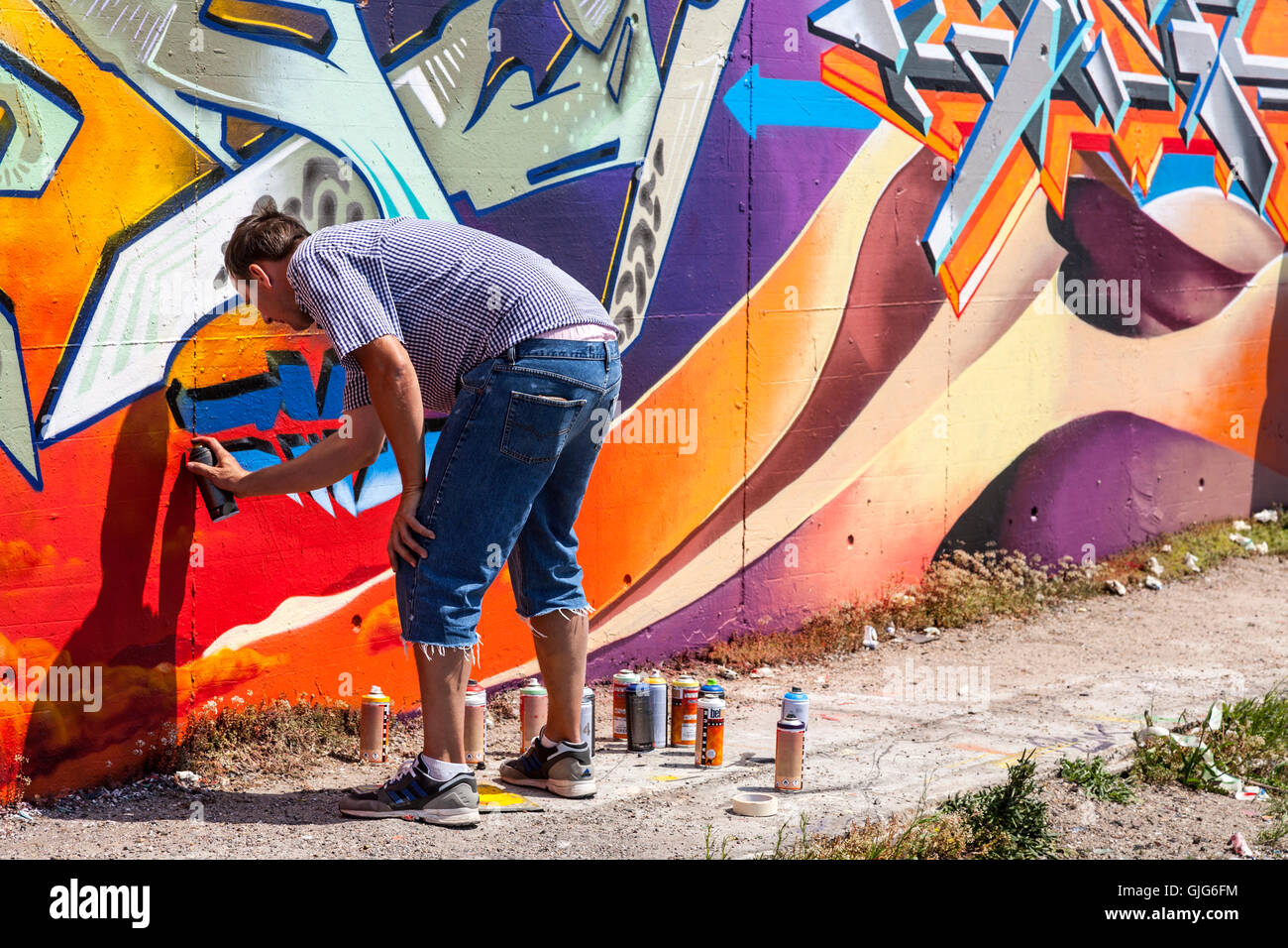 Graffiti artist hard at work painting an old wall, Friedrichshain, Berlin, Germany. Stock Photo
