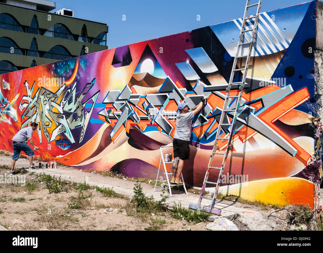 Graffiti artists hard at work painting an old wall, Friedrichshain, Berlin, Germany. Stock Photo