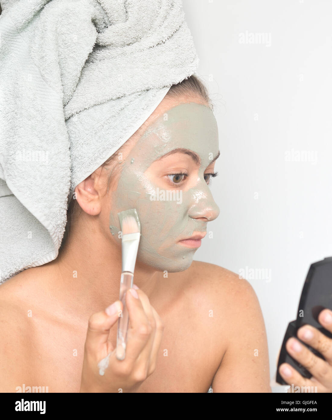 young woman applying facial clay mask to her face using brush Stock Photo