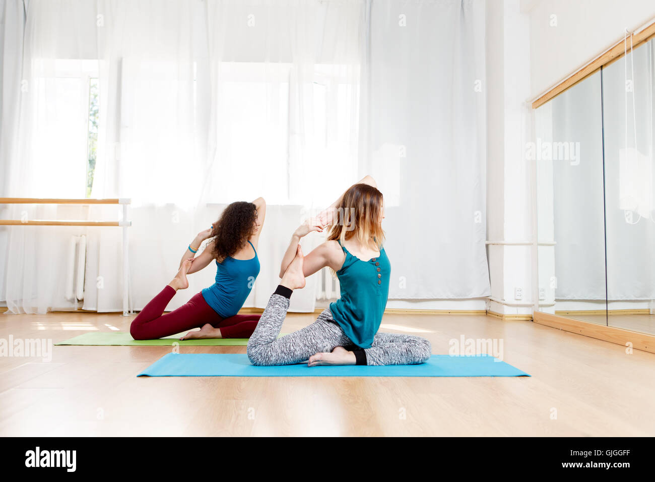 Side view portrait of two young women practice pigeon pose Stock Photo