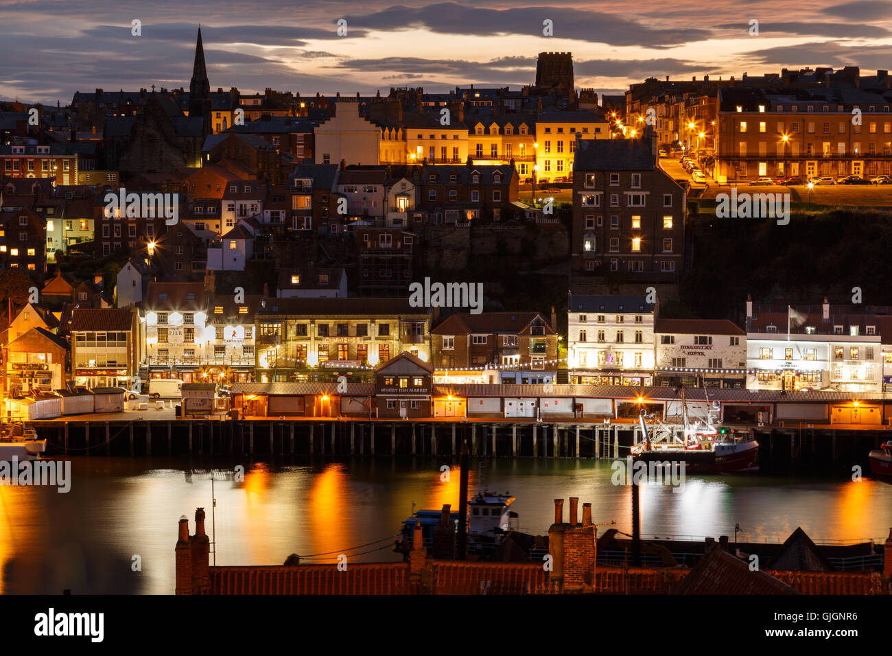 Whitby harbour and town, at night, with a dramatic sunset behind. In