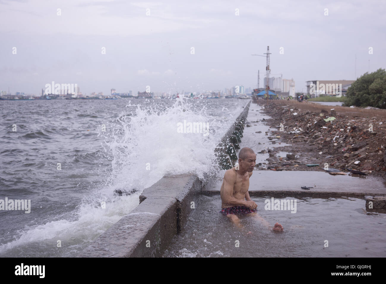 North Jakarta, Indonesia. 16th Aug, 2016. Aseng, 42, bath behind the old concrete sea-wall as waves smash into it. Jakarta sinking by between 7.5 and 17 centimetres a year, more than 10 times faster than the sea is rising. Governments will split the 3.2 trillion rupiah ($263 million) cost for the first 8 kilometres of the wall. Developers would put up the remaining 24 kilometres by 2030 in exchange for the right to build on reclaimed land. © Anton Raharjo/Pacific Press/Alamy Live News Stock Photo