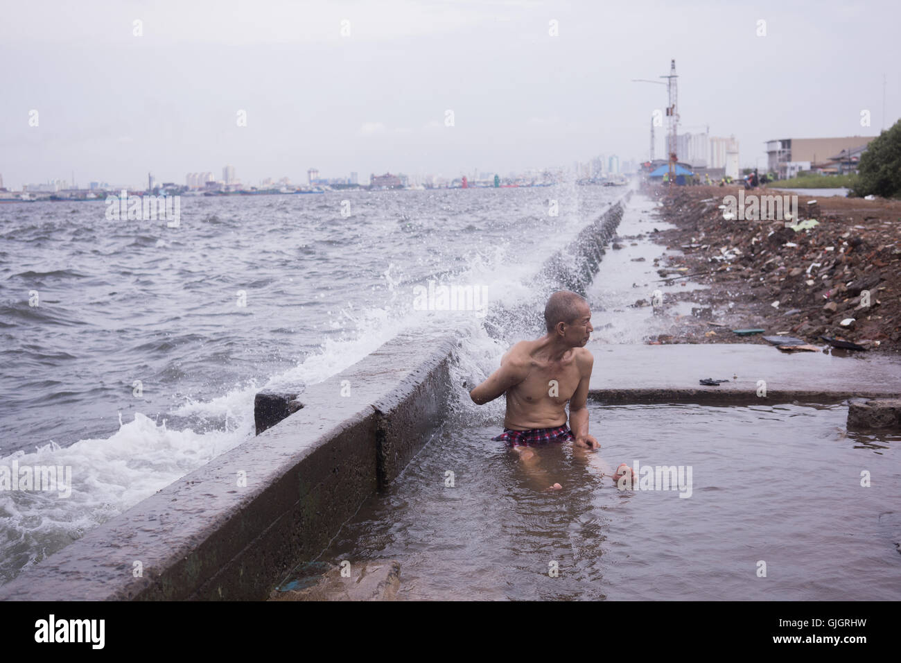 North Jakarta, Indonesia. 16th Aug, 2016. Aseng, 42, bath behind the old concrete sea-wall as waves smash into it. Jakarta sinking by between 7.5 and 17 centimetres a year, more than 10 times faster than the sea is rising. Governments will split the 3.2 trillion rupiah ($263 million) cost for the first 8 kilometres of the wall. Developers would put up the remaining 24 kilometres by 2030 in exchange for the right to build on reclaimed land. © Anton Raharjo/Pacific Press/Alamy Live News Stock Photo