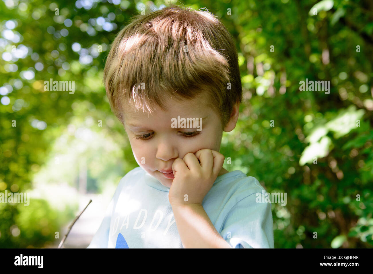 Boy standing in garden with hand on chin Stock Photo