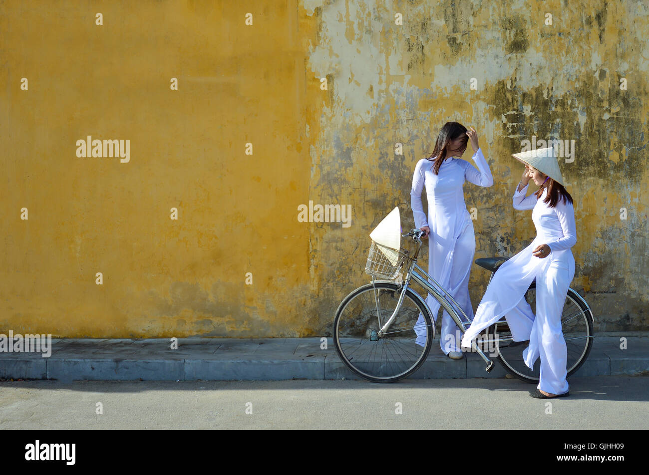 Two women in traditional clothing standing in street talking, Hoi An, Vietnam Stock Photo