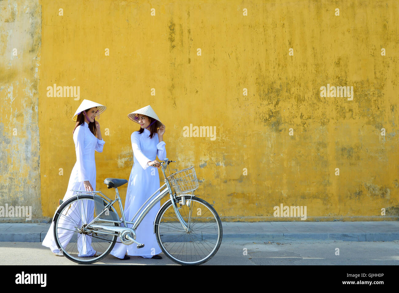 Two women in traditional clothing standing in street talking, Hoi An, Vietnam Stock Photo