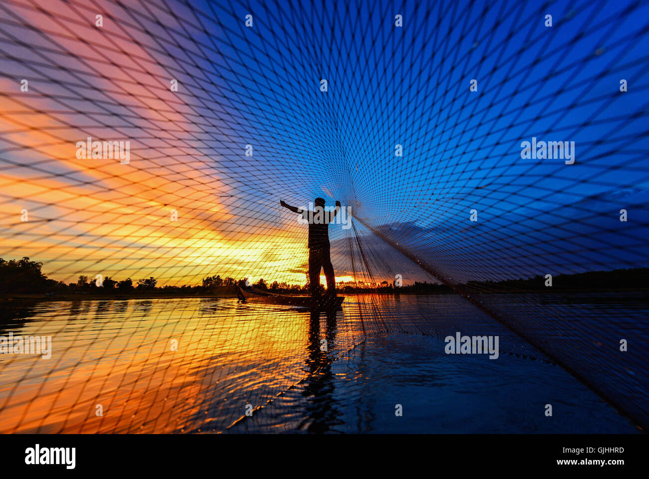 Fisherman casting fishing net at sunset, Thailand Stock Photo