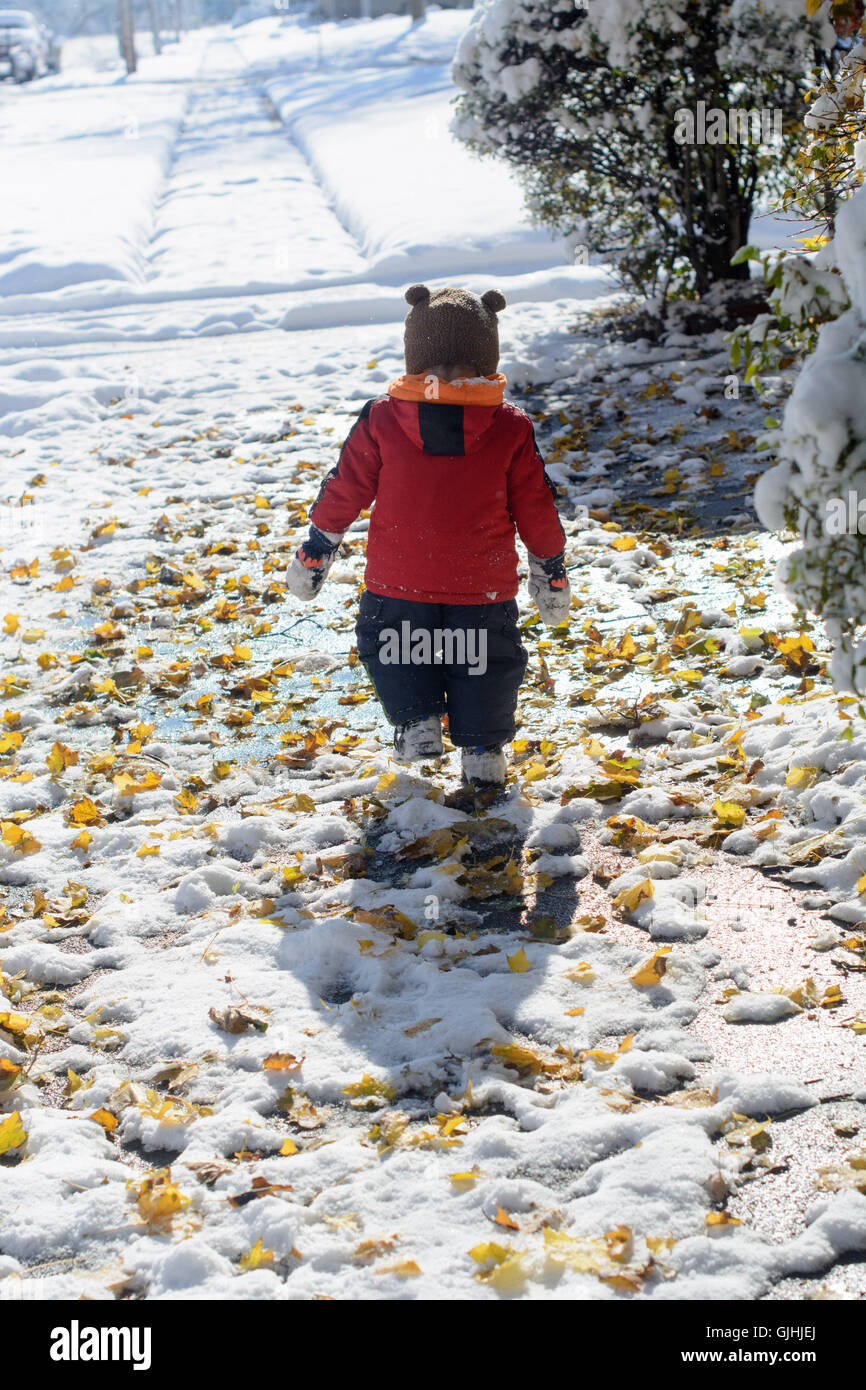 Rear view of boy walking down street in snow Stock Photo
