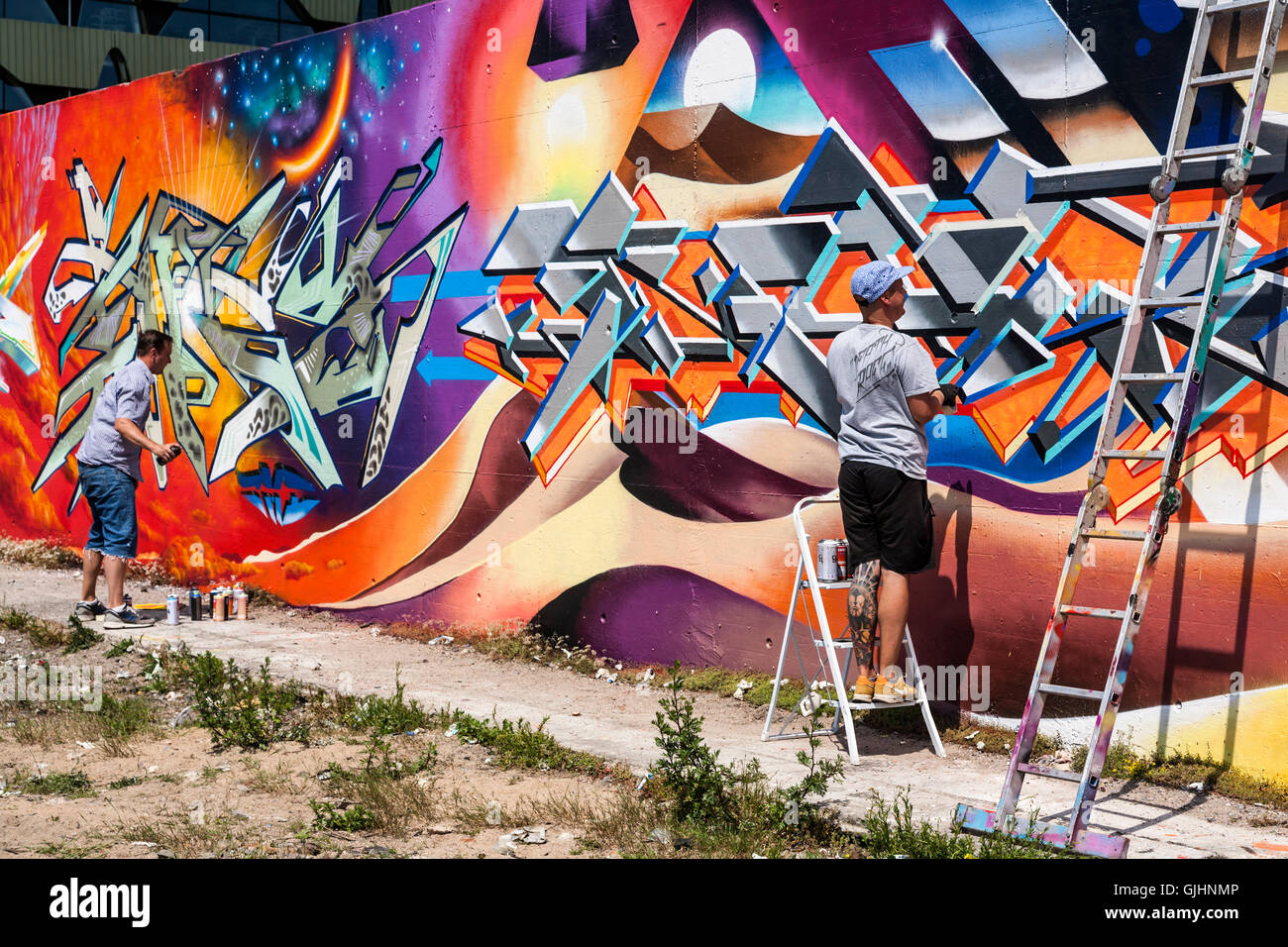 Graffiti artists hard at work painting an old wall, Friedrichshain, Berlin, Germany. Stock Photo