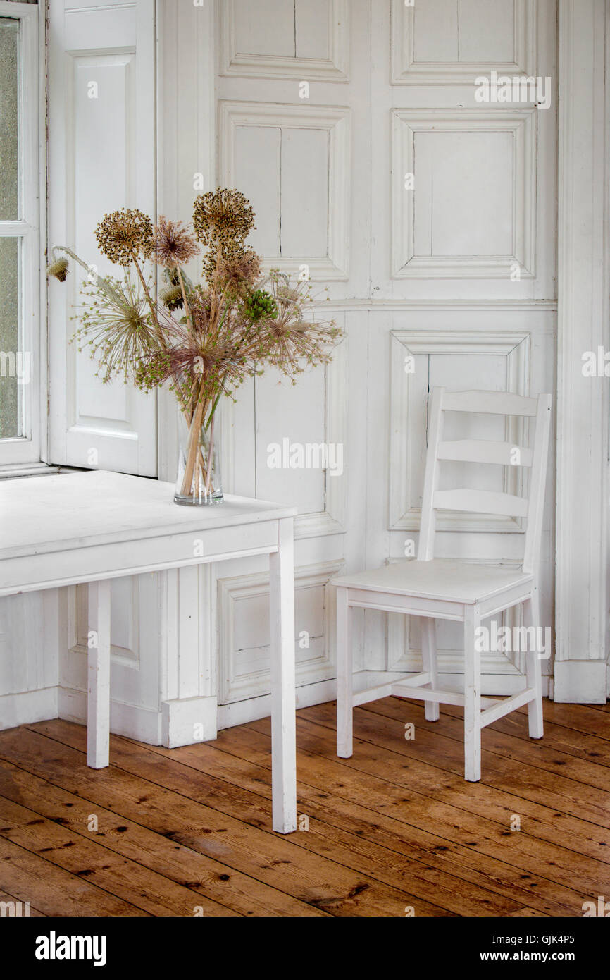 White room, chair & table with wooden floor and a vase of flowers Stock Photo