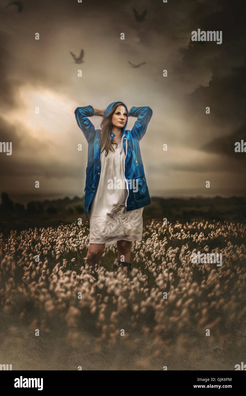 young woman in blue rain jacket standing in fields Stock Photo