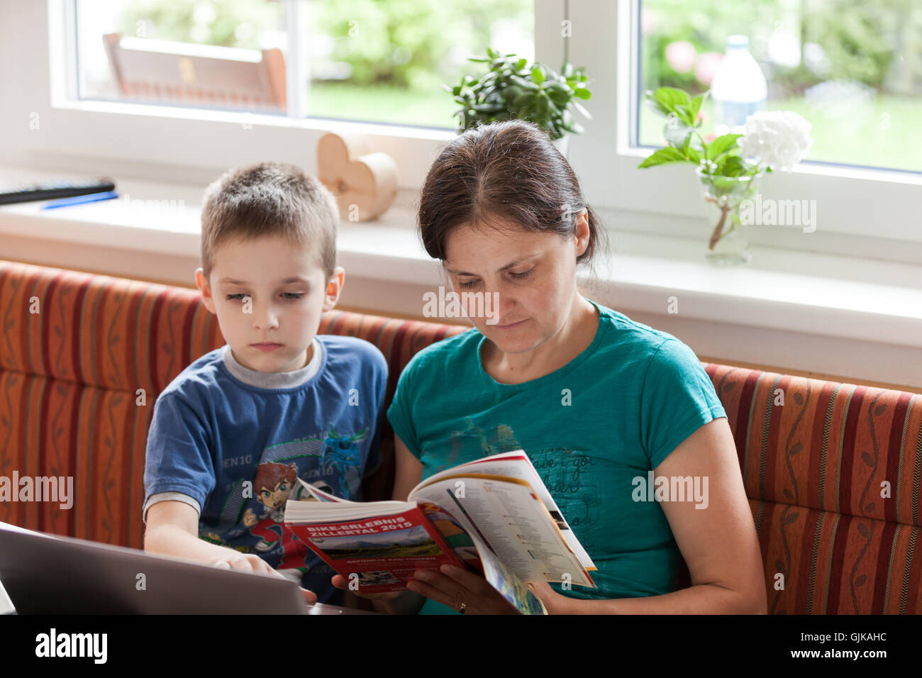 Young boy and mother with computer and tourist brochure in the kitchen studying the tour for holiday Stock Photo