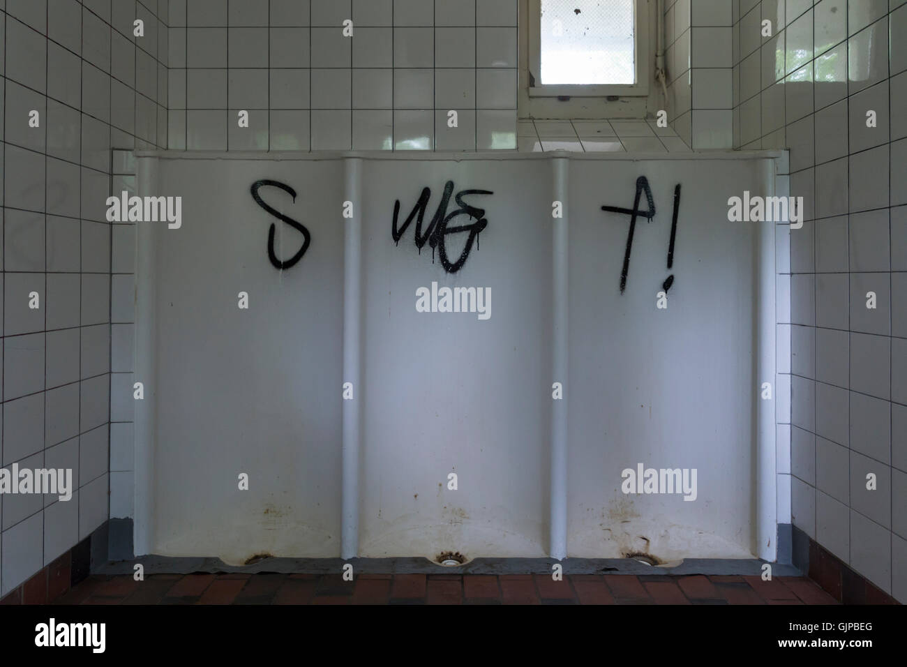 A dirty public toilet with three mens urinals and black graffiti Stock Photo