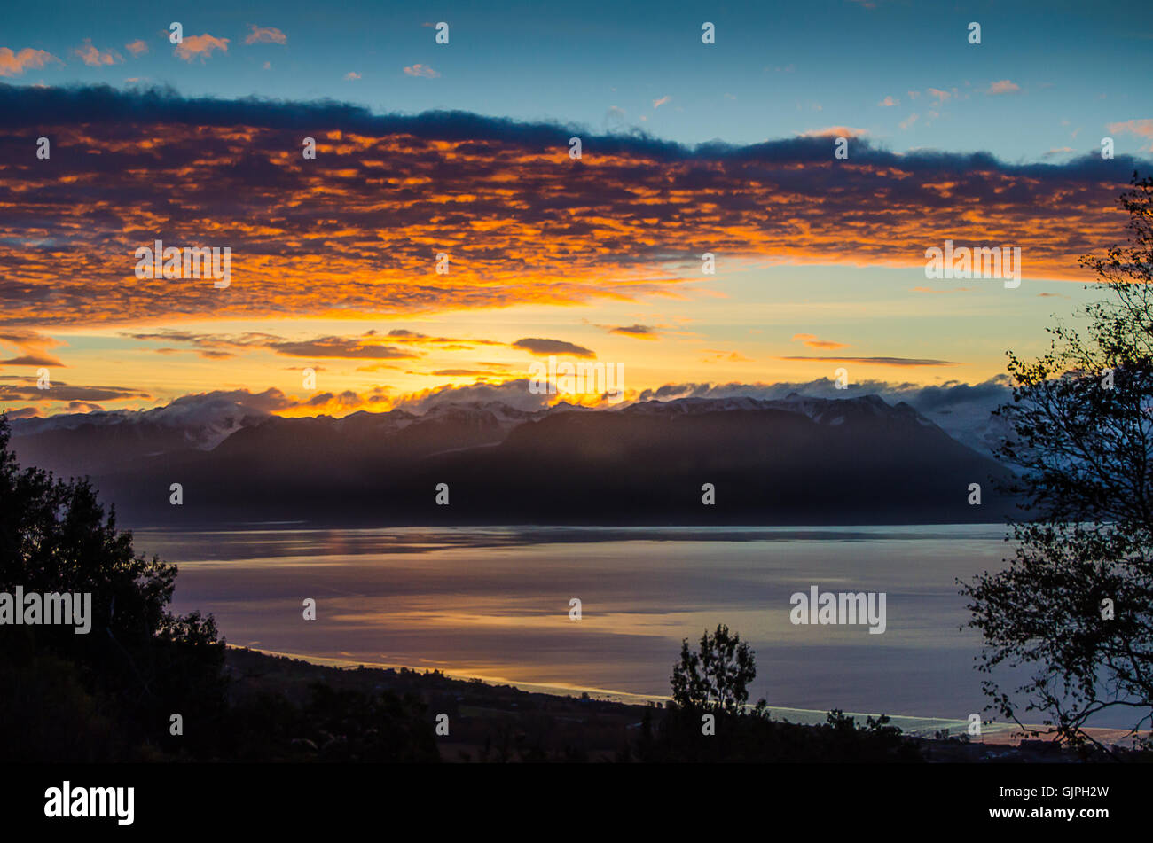 A bank of clouds glow with morning light as the sun tries to raise over the Kenai Mountains and Kachemak Bay is also glowing Stock Photo