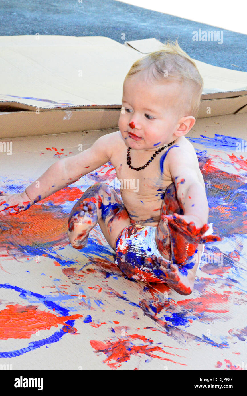 Toddler Finger Painting Outdoors on a Lage Piece of cardboard.. Stock Photo