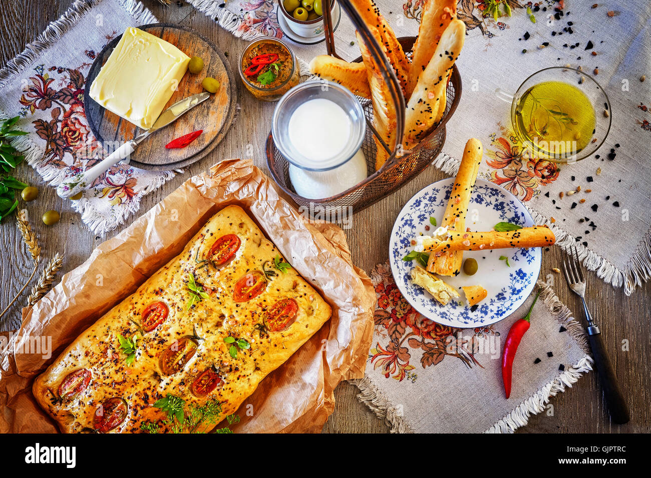 Traditional focaccia in baking paper and bread sticks, rustic setting on a wooden table from above. Stock Photo