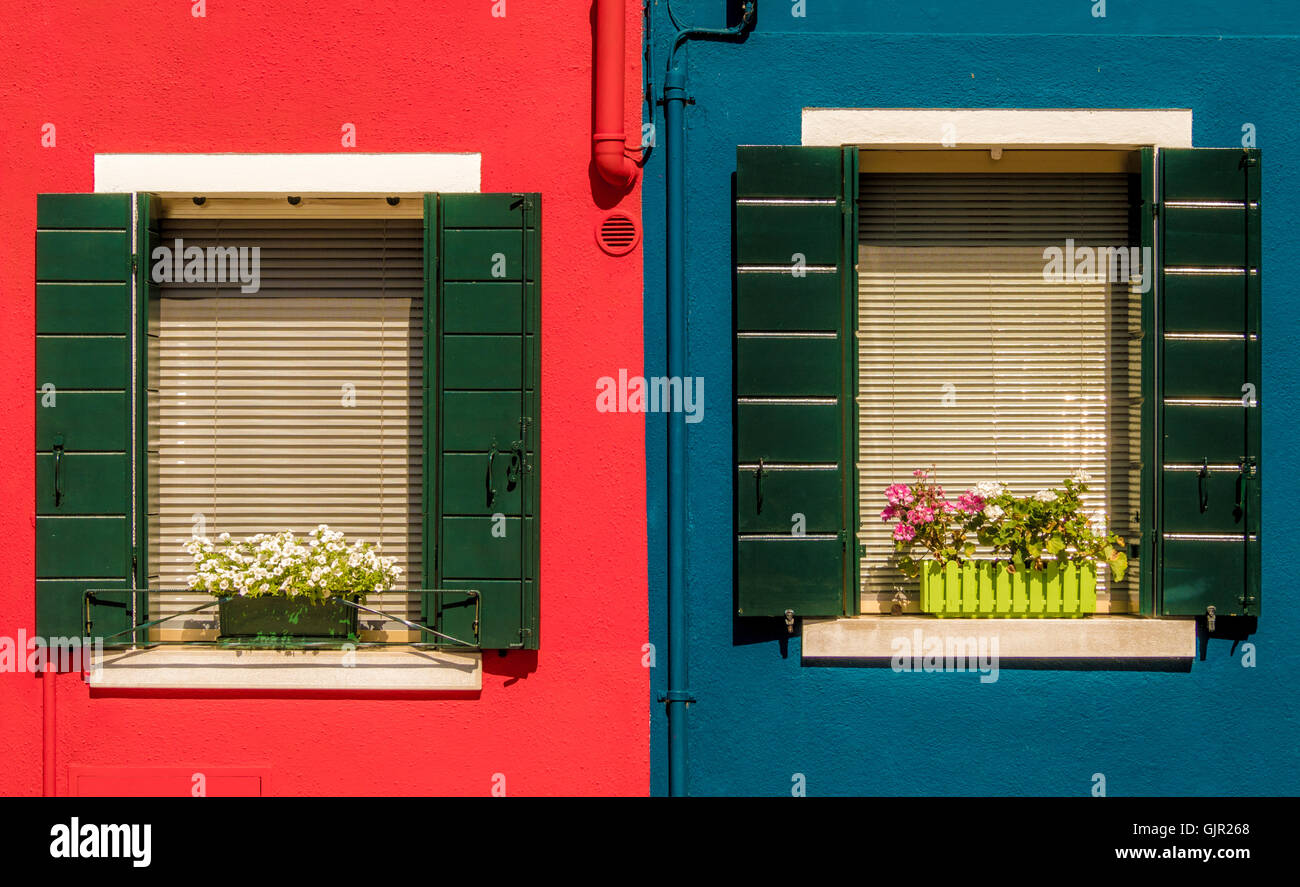Dark green window shutters on a bright red and blue rendered exterior wall of traditional houses on the island of Burano. Italy. Stock Photo