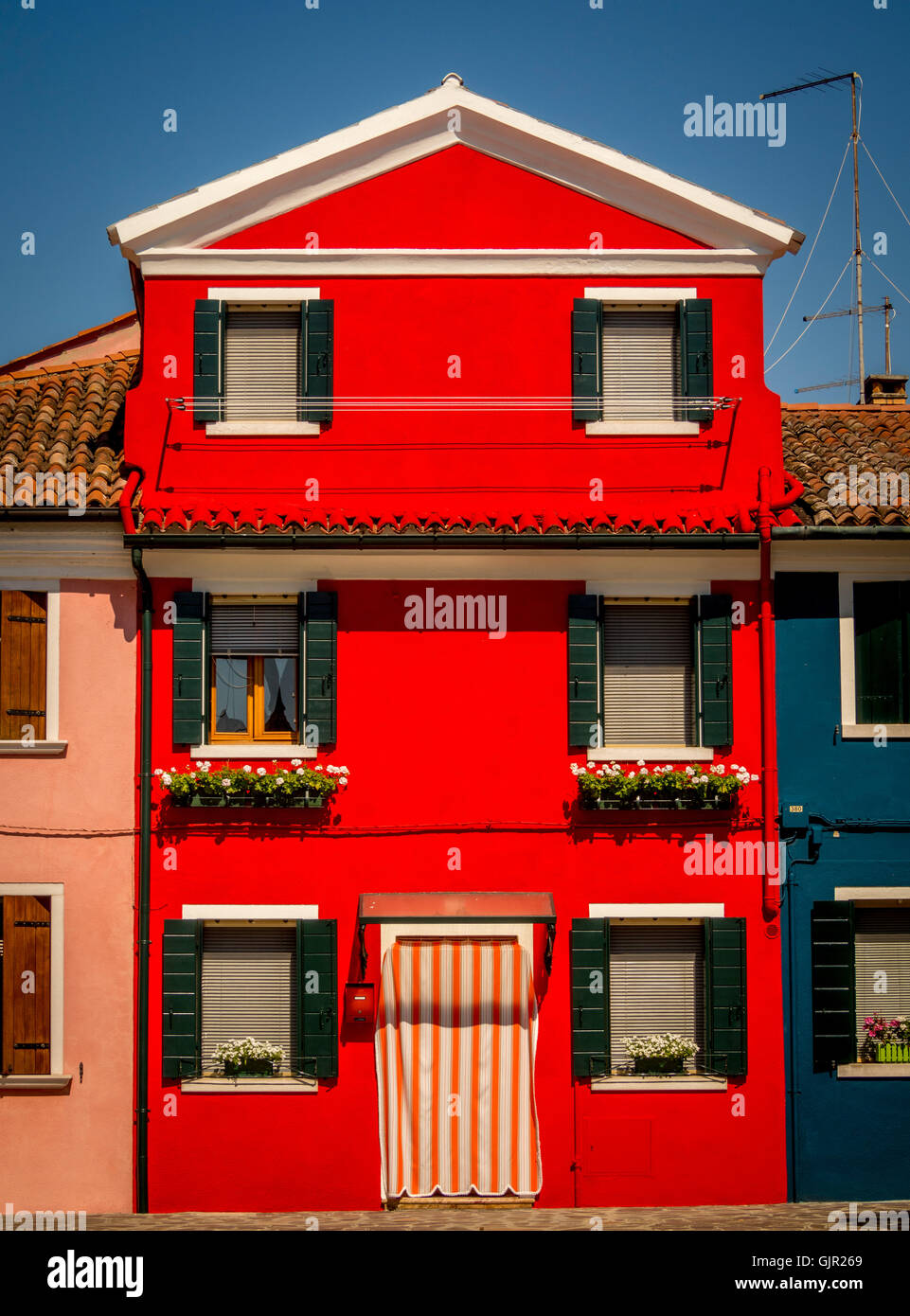 Dark green window shutters on a bright red rendered exterior wall of traditional house on the island of Burano. Italy. Stock Photo
