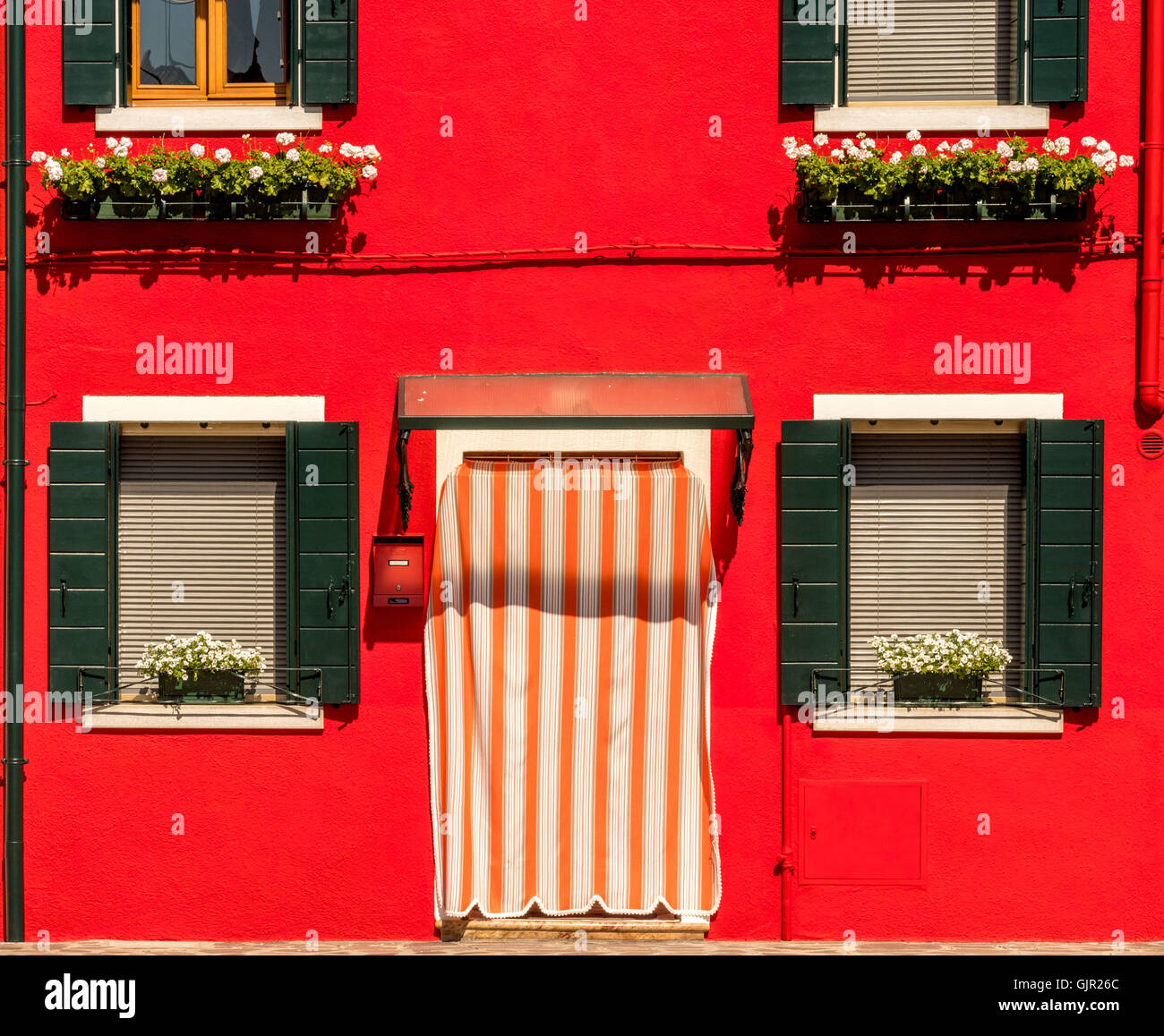 Dark green window shutters on a bright red rendered exterior wall of traditional house on the island of Burano. Italy. Stock Photo