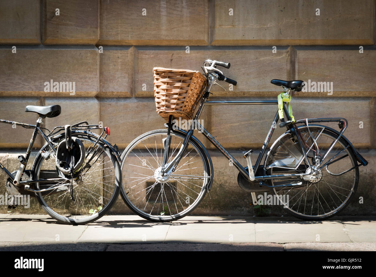 Traditional bicycle with basket leaning against the old stone wall of a a  college at Cambridge University UK in side light Stock Photo - Alamy