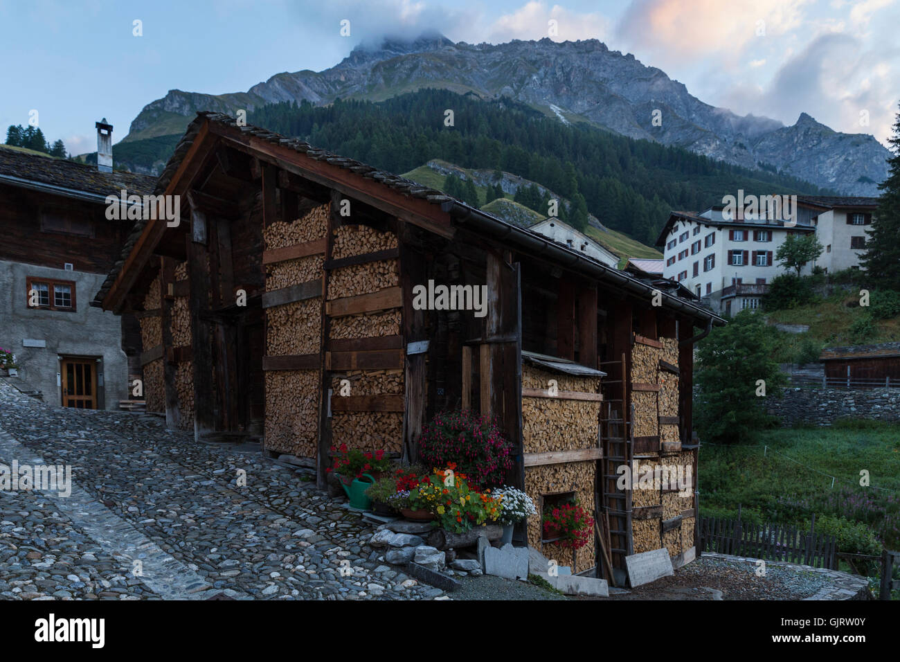 View on an old wooden house with neatly stacked firewood in front in the town of Splugen in Switzerland. Stock Photo