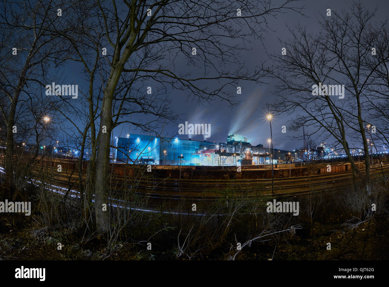 Steelplant in Duisburg, Germany, at night with trees and railways in the front - surreal scenery Stock Photo