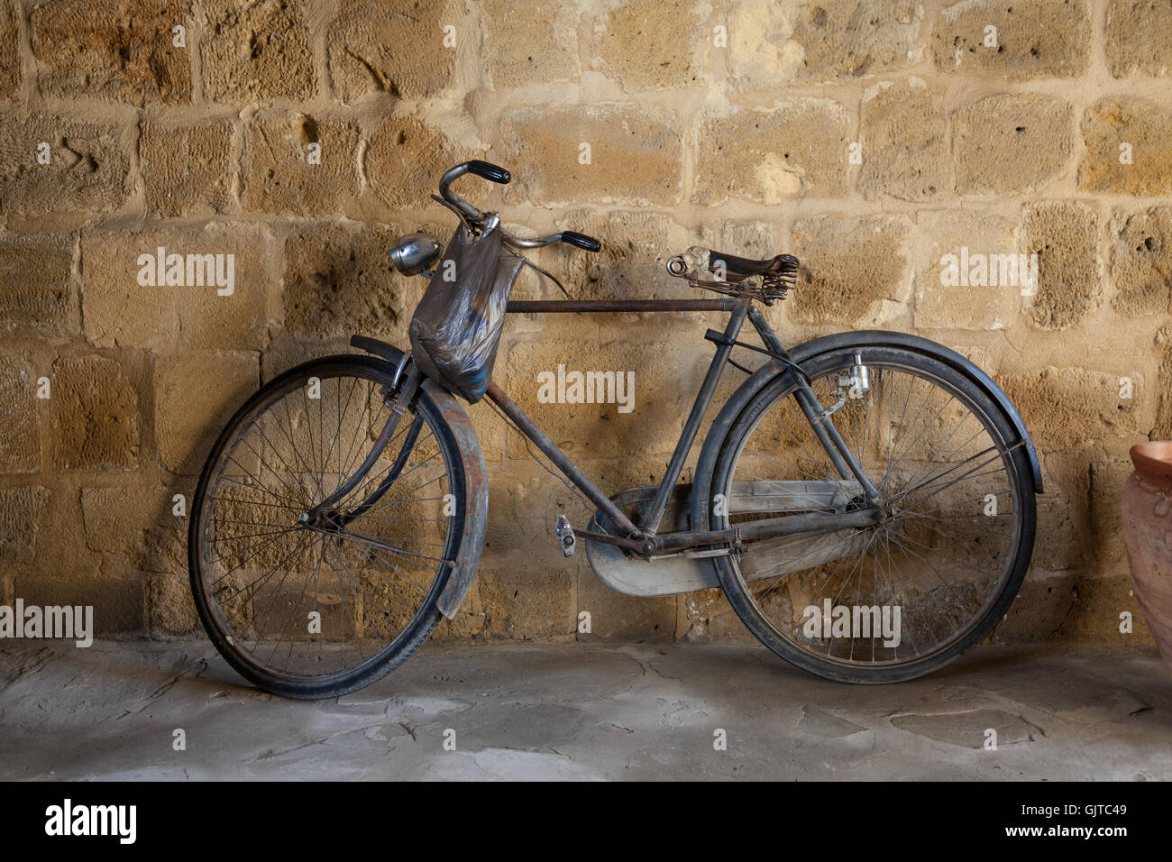 An old pedal bike leans against a stone wall. A bag hangs from the handlebars Stock Photo