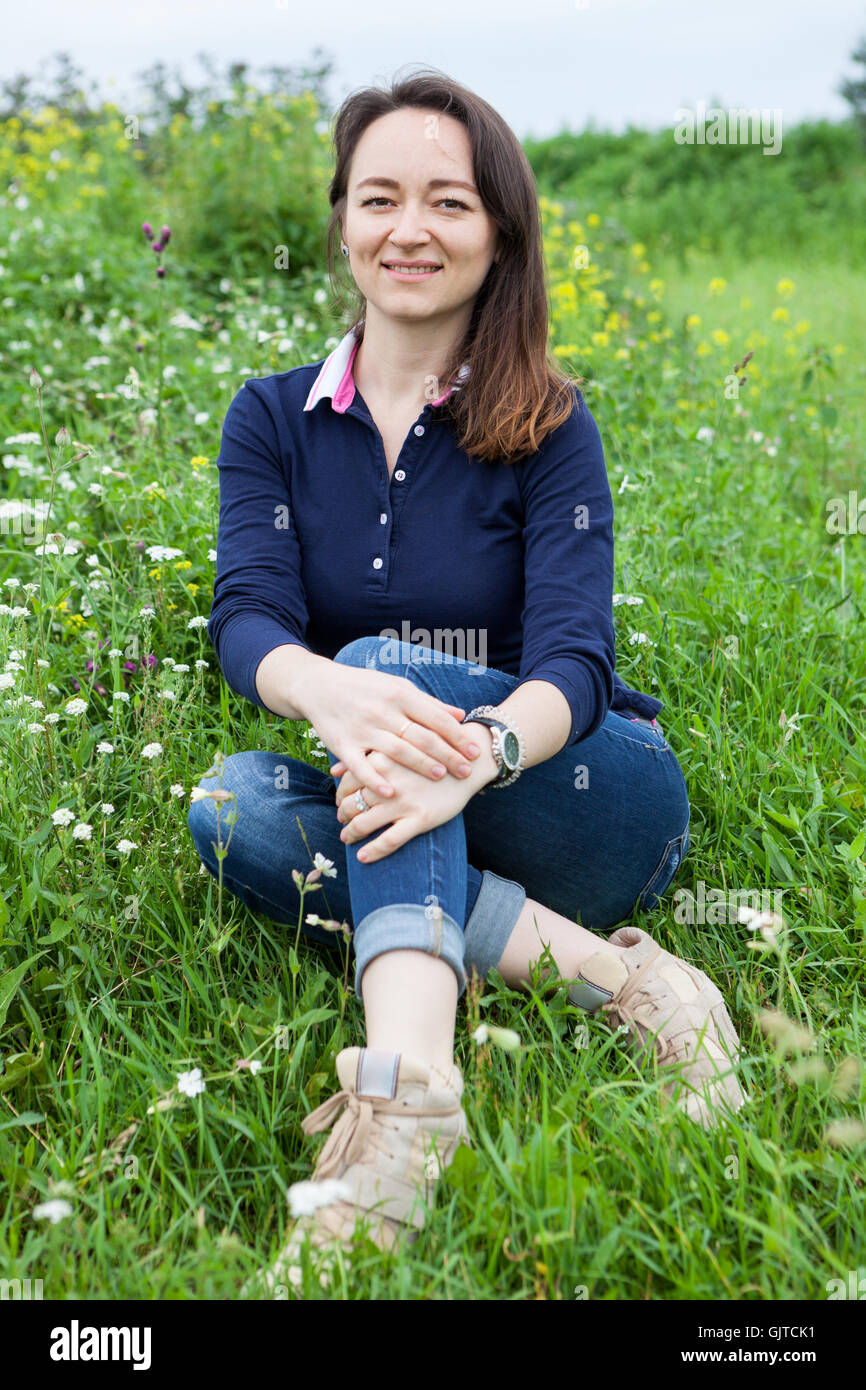 Portrait of smiling beautiful woman sitting on green grass at summer ...
