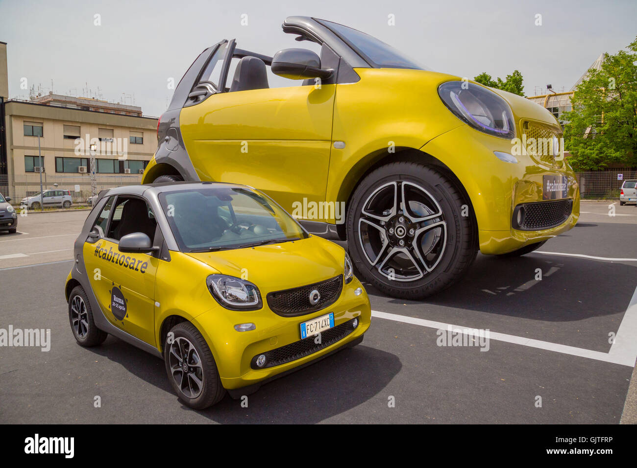 A giant Smart car next to a standard size Smart car in Rome Featuring