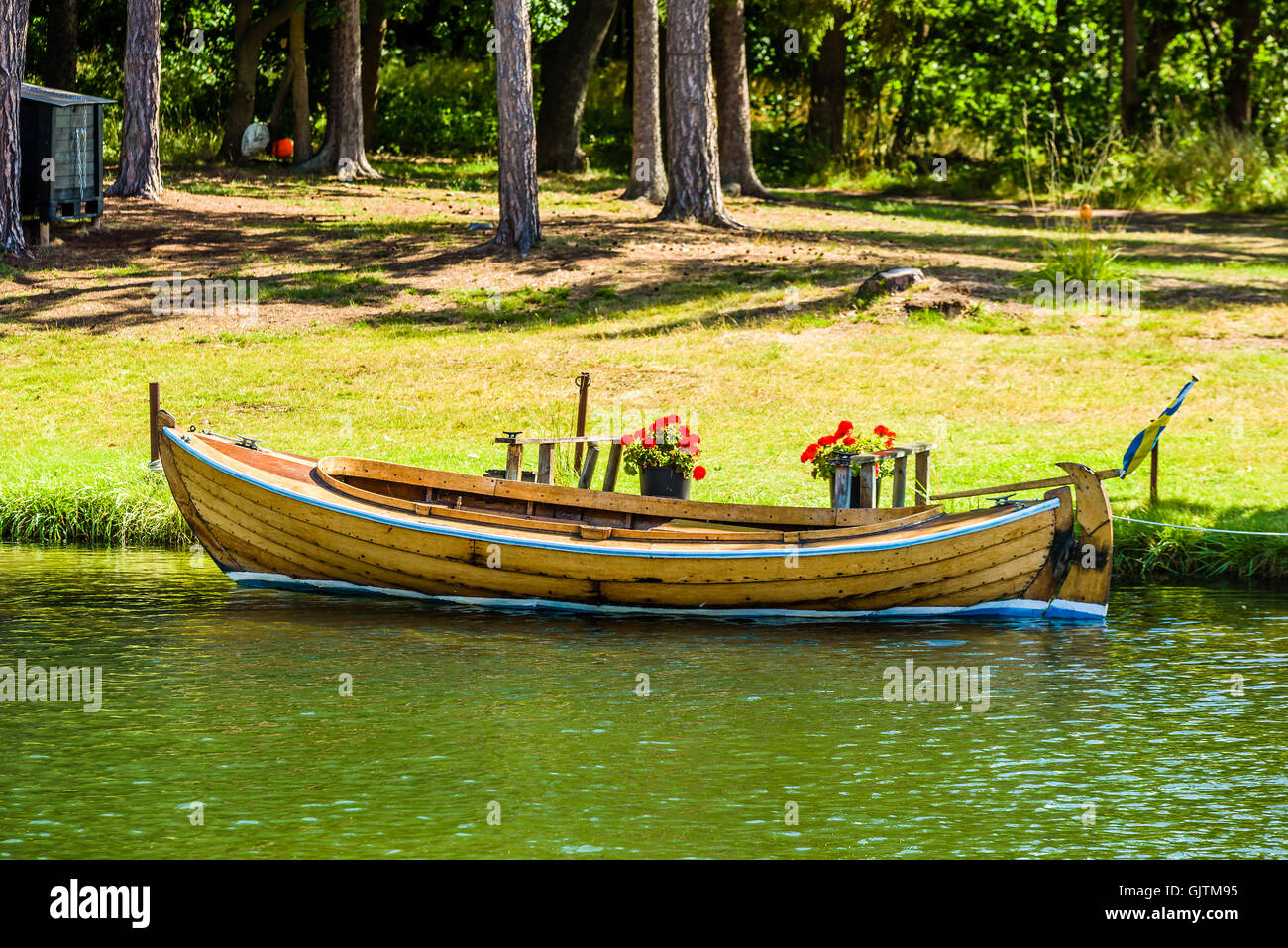 Old wooden motorboat moored by the shore with pine trees and grass in the background. Stock Photo