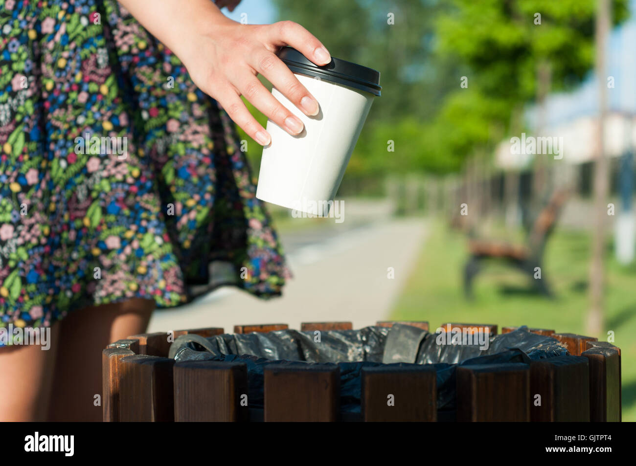 Close-up female hand throwing paper cup on trash bin outside in park ...