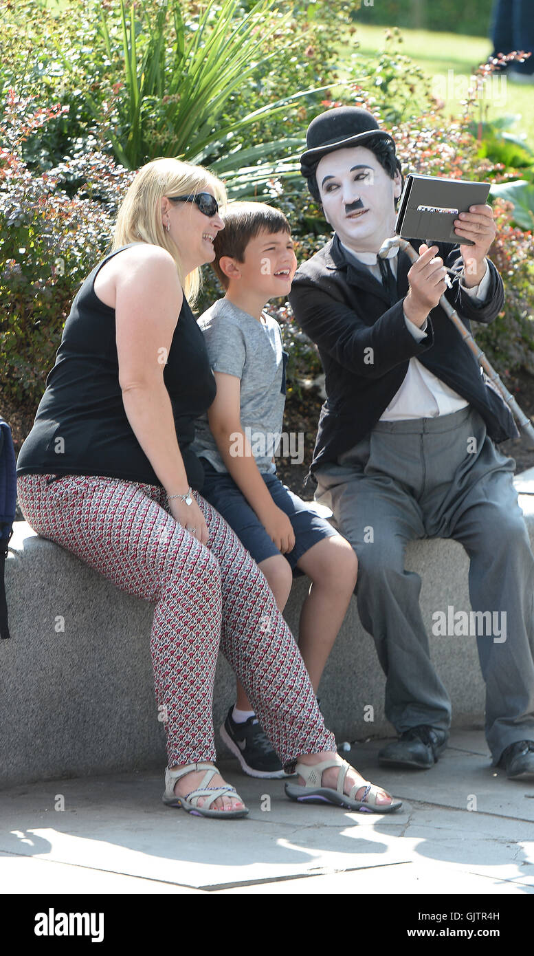 A woman and her son have their picture taken with a Charlie Chaplin look-alike on London's South Bank, as the warm weather continues. Stock Photo