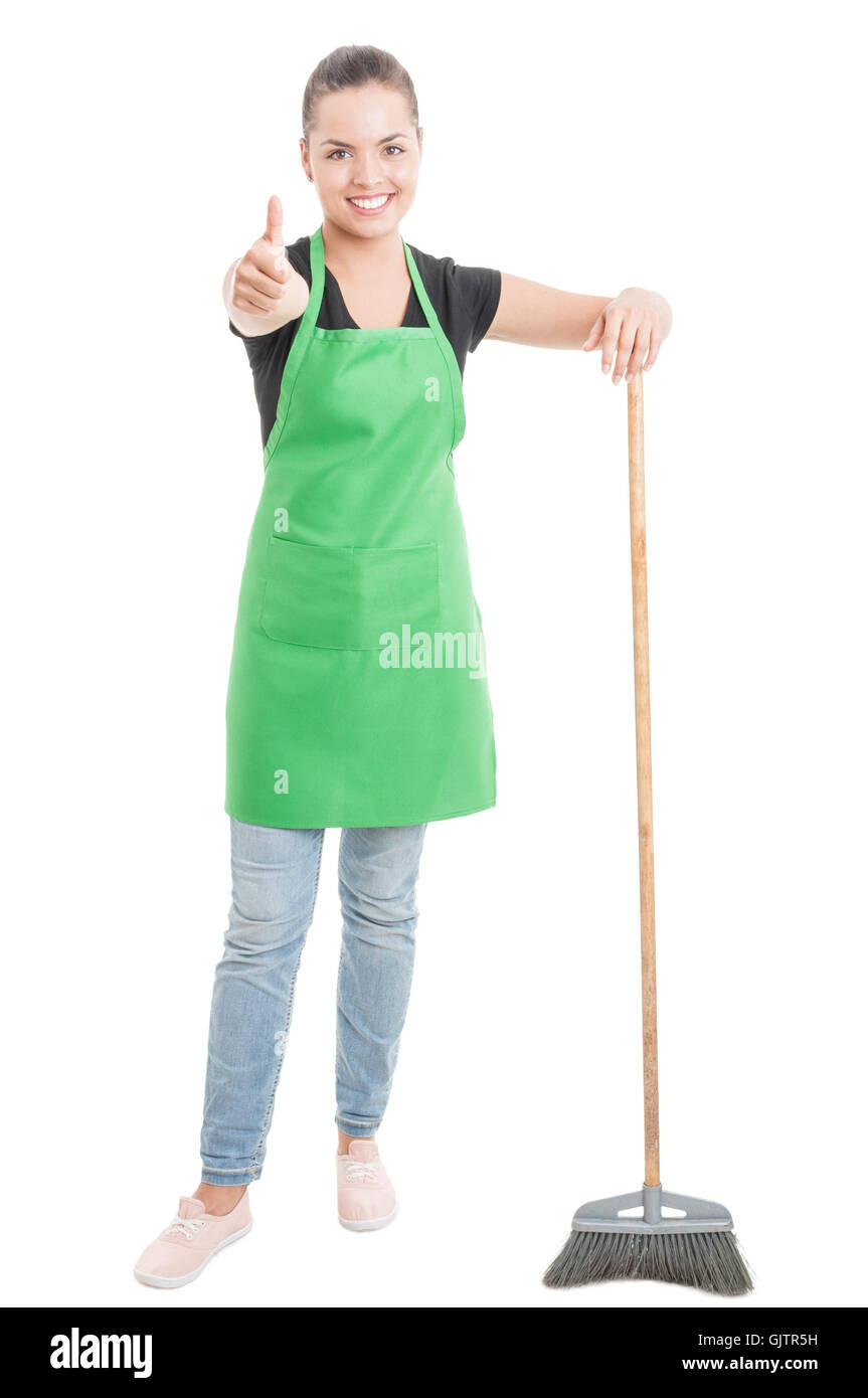 Young female showing thumb up while sweeping the floor isolated on