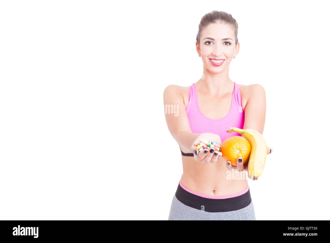 Girl wearing sportswear showing fruits and pills or supplements isolated on white background with copy text space Stock Photo