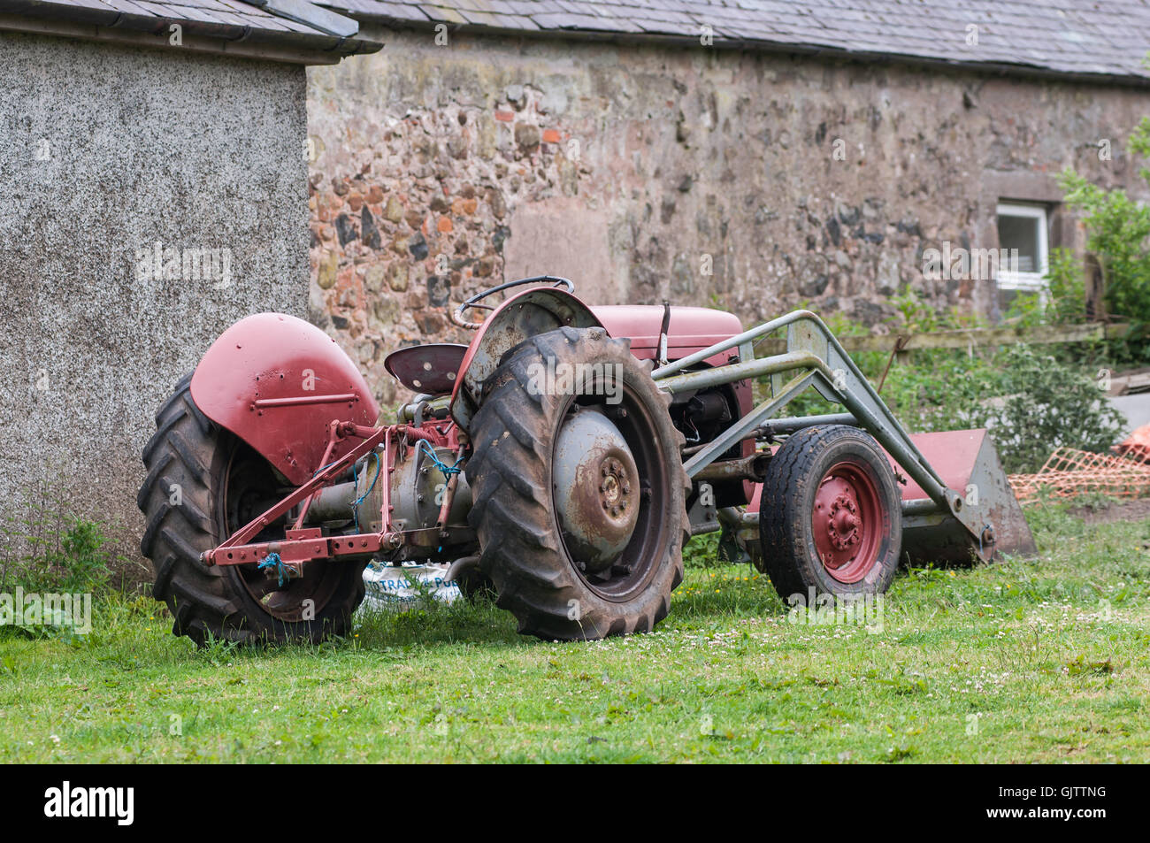 An old red tractor parked beside an old building or shed Stock Photo ...