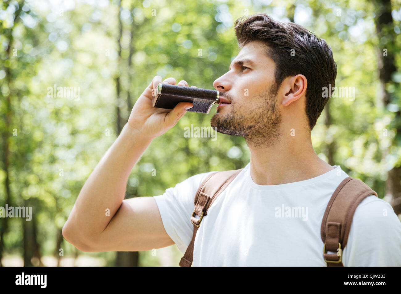 Handsome young man with backpack standing and drinking from flask in
