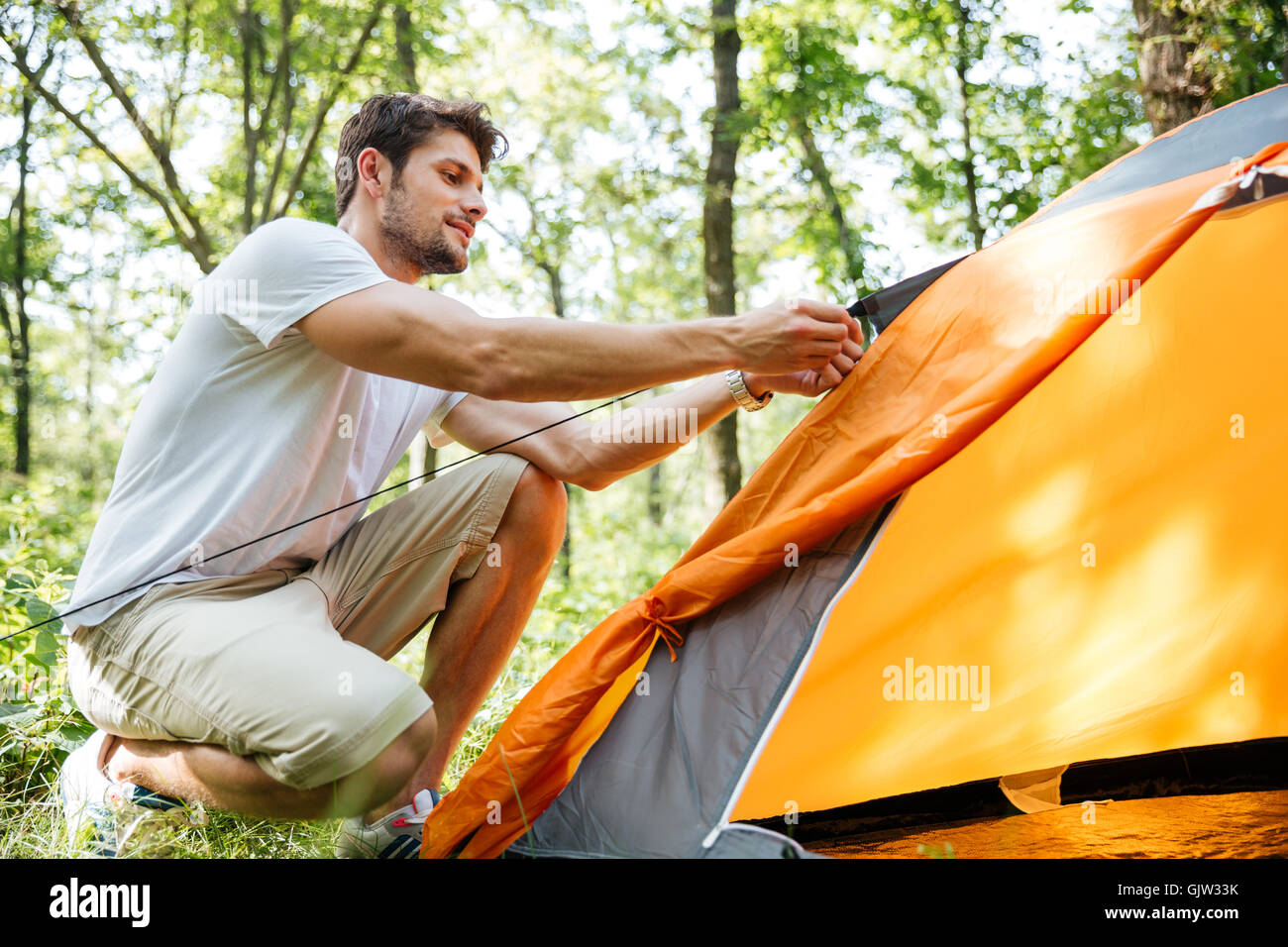 Handsome young man tourist setting up touristic tent in forest Stock Photo
