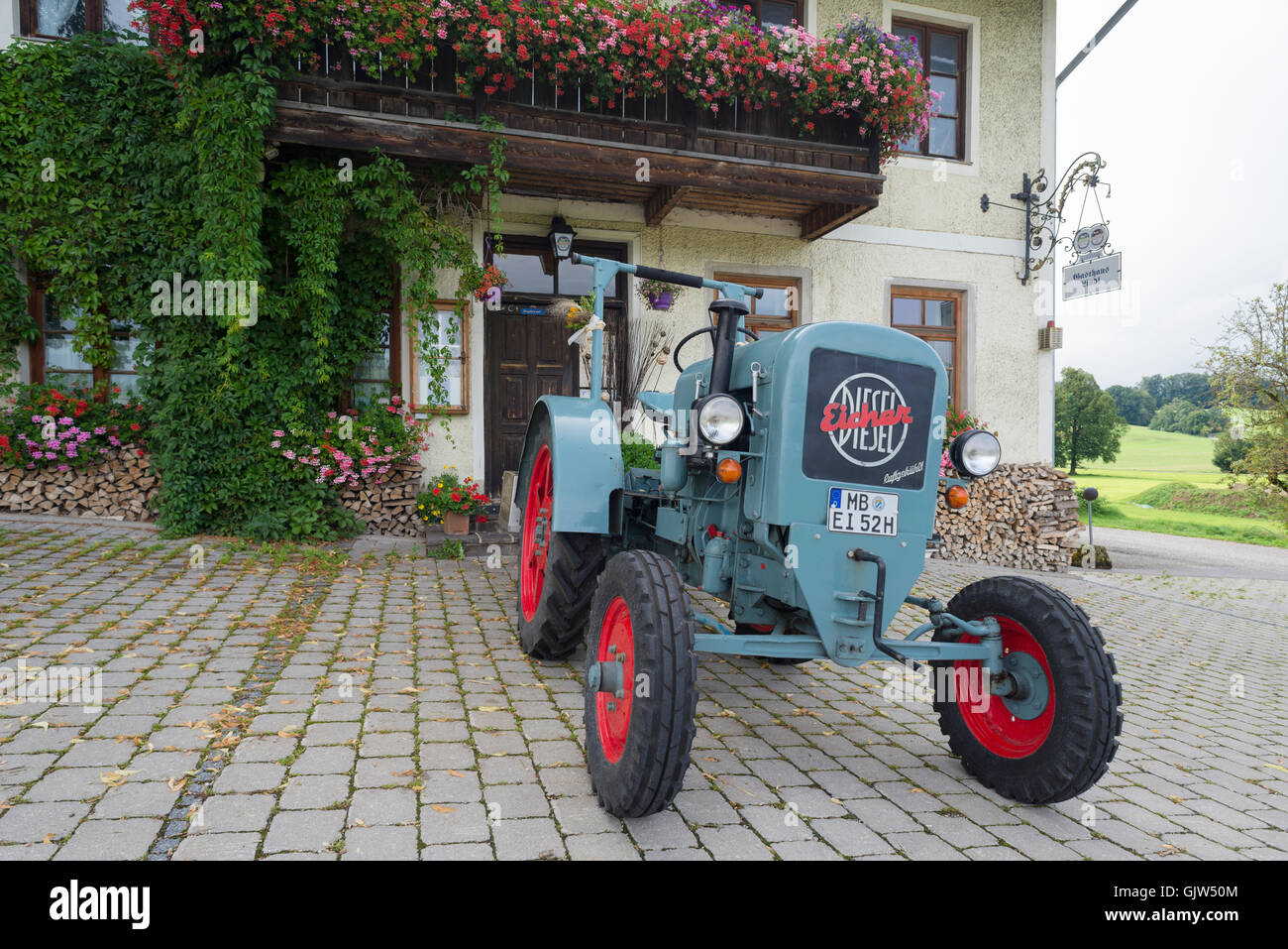 Eicher Diesel vintage tractor parked in front of the Lindl inn covered with blooming geraniums, Bavaria, Germany Stock Photo