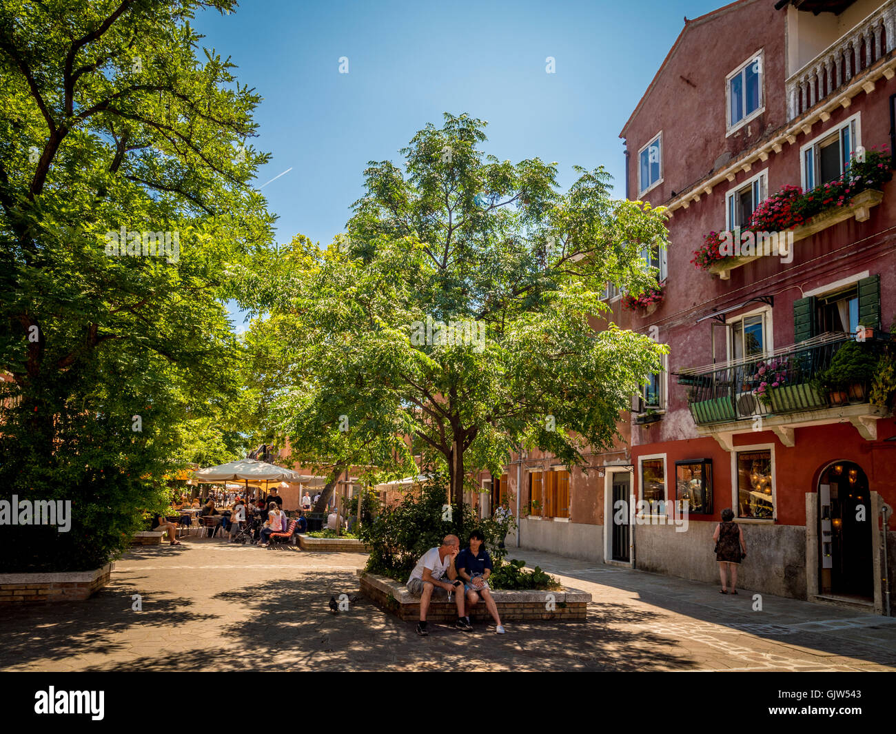Couple sitting in the shade of tree, in a square in Murano, Italy. Stock Photo