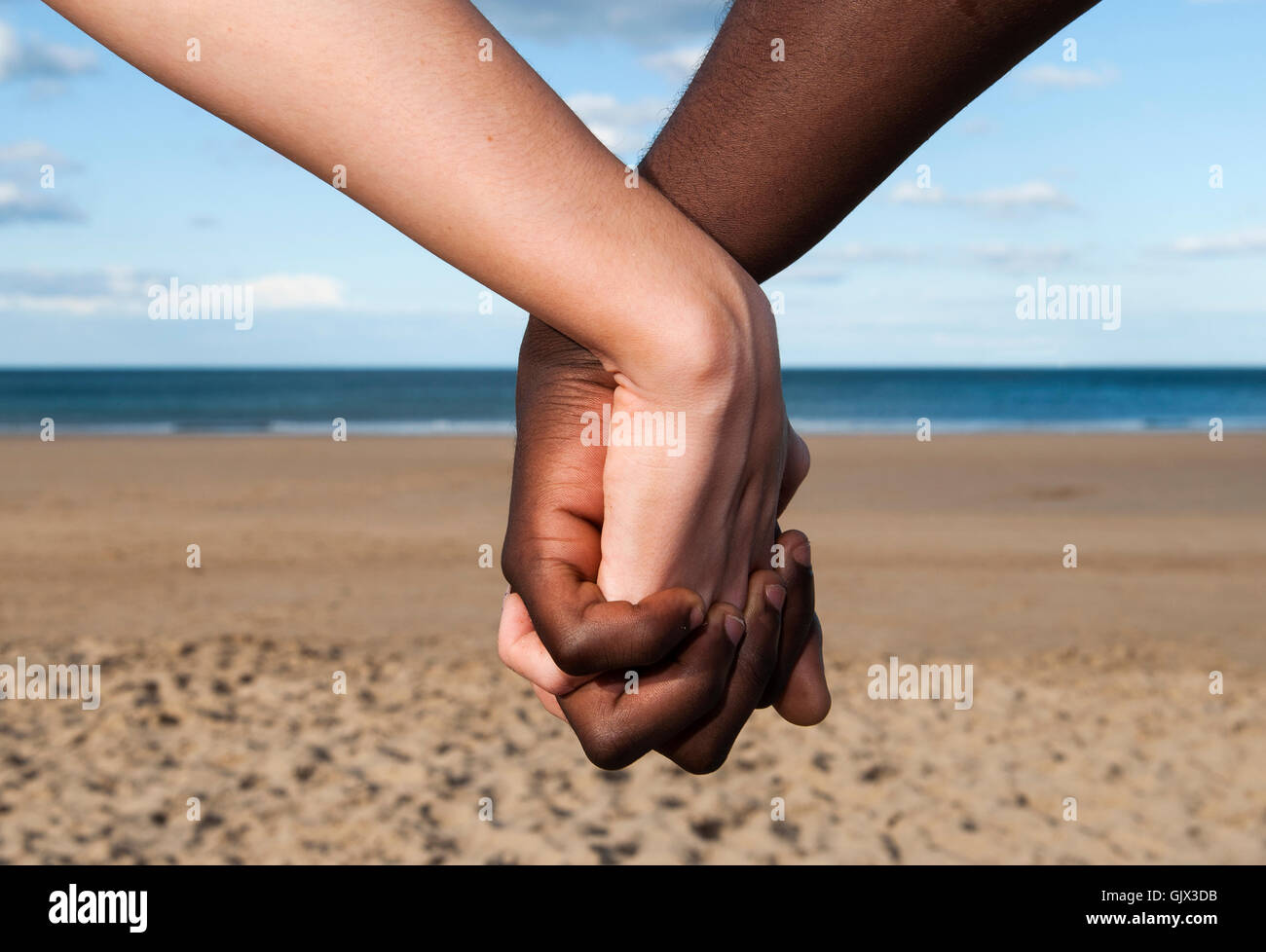 Holding hands mixed race couple  close up  male  & female  multicultural sea and sand  together  love  peace symbol concept Stock Photo