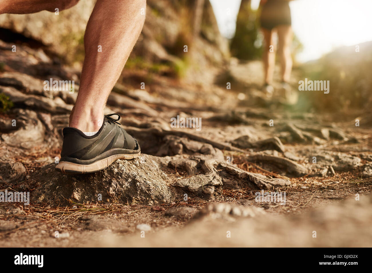 Closeup of man trail running on rocky terrain. Low section of male runner on cross country run. Stock Photo