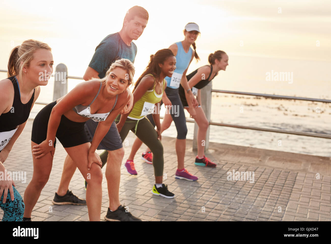 Shot of athletes at the starting point of a marathon. Diverse group of people running together on seaside promenade. Stock Photo