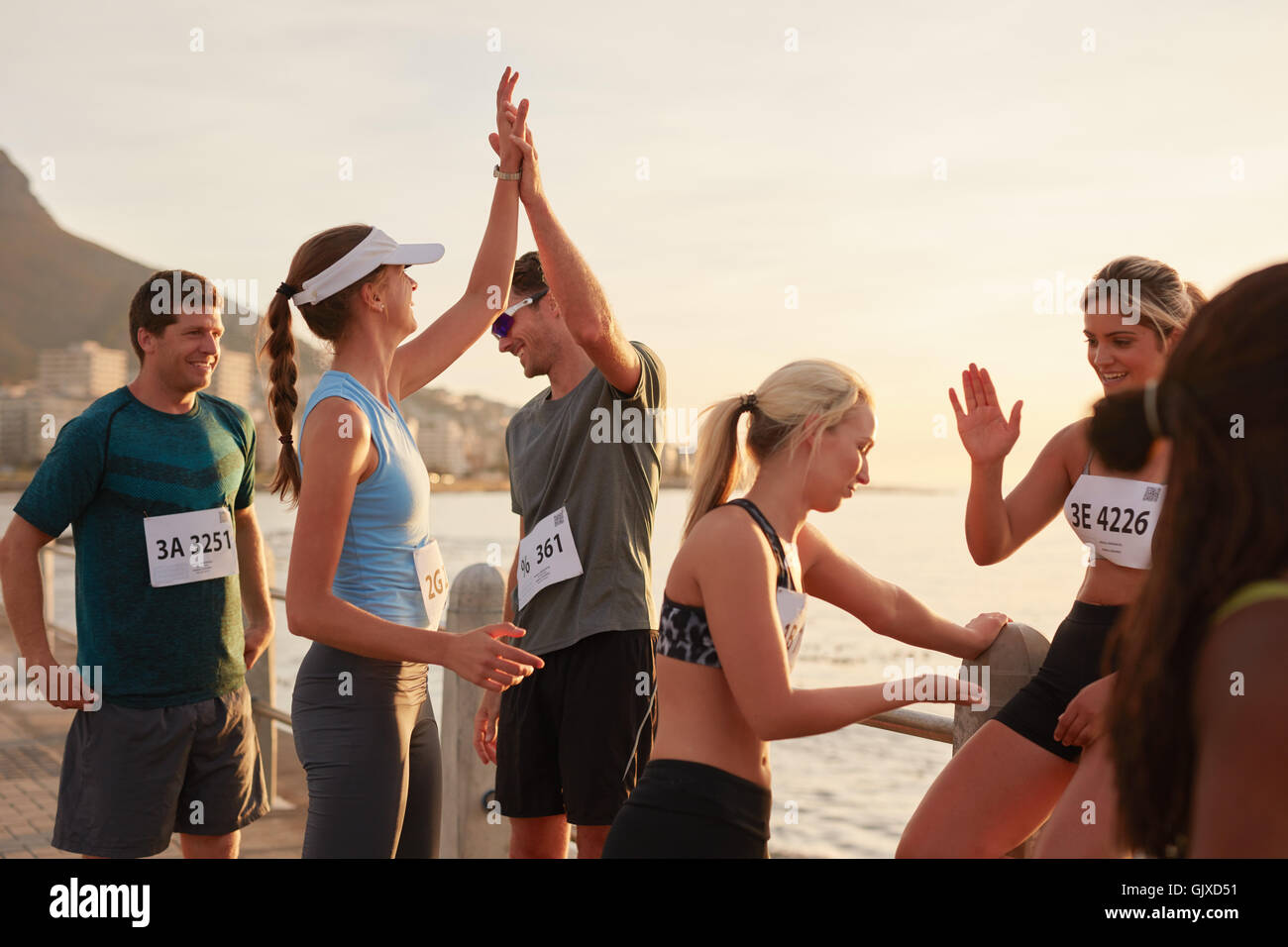 Runners giving high five to each other after a training session. Group of athletes celebrating success after a race. Stock Photo