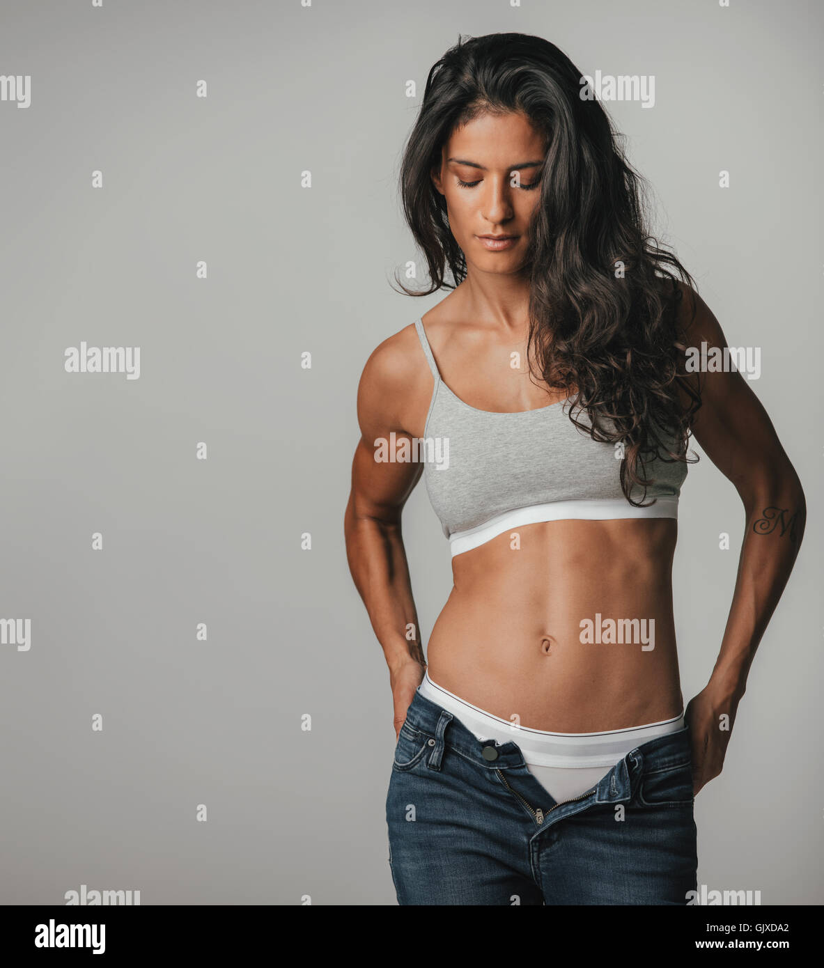 Fit young woman pulling down pants with copy space to her side over gray background Stock Photo