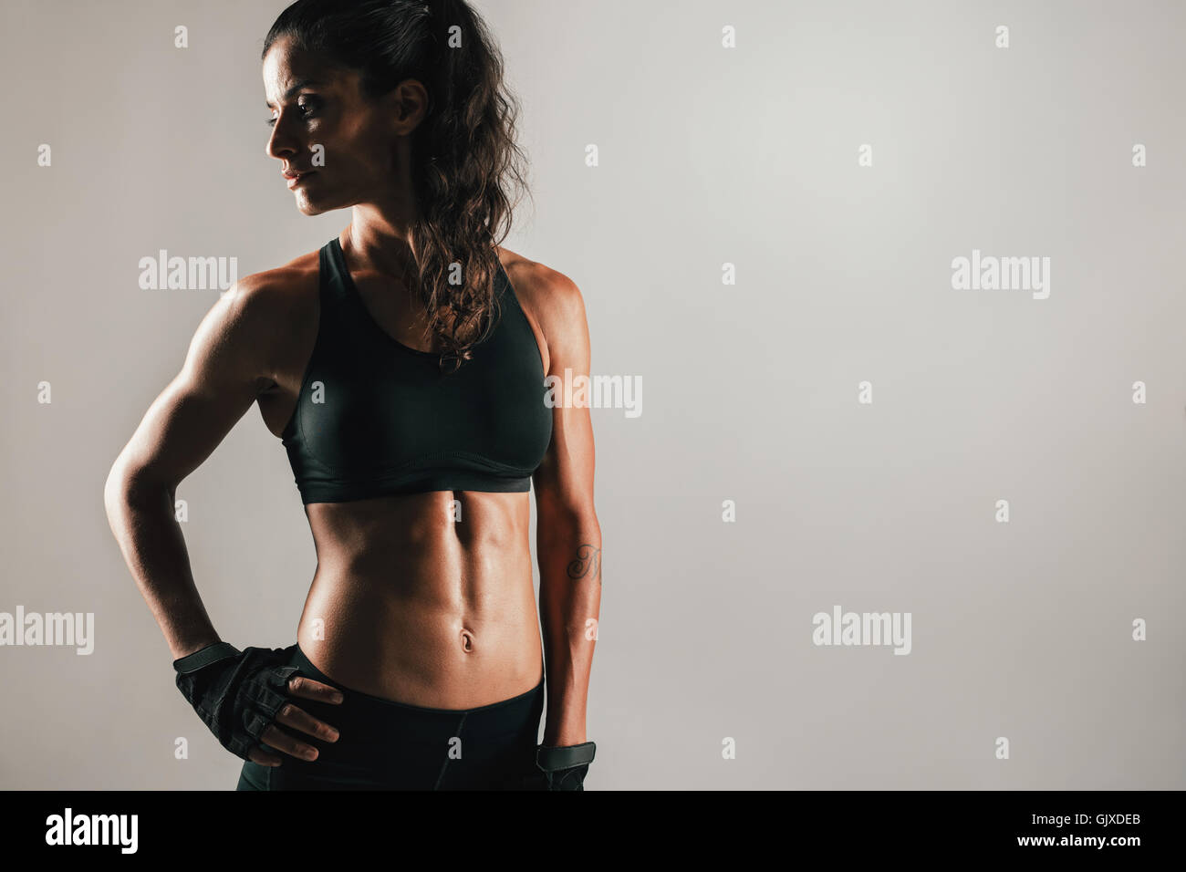 Muscular woman in shadow with gloved hand on hip and spotlight on firm abdominal muscles Stock Photo