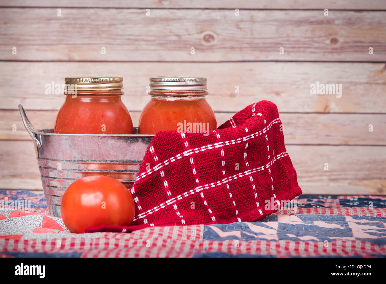 Jars of tomato sauce sit in a metal tin with a fresh tomato Stock Photo