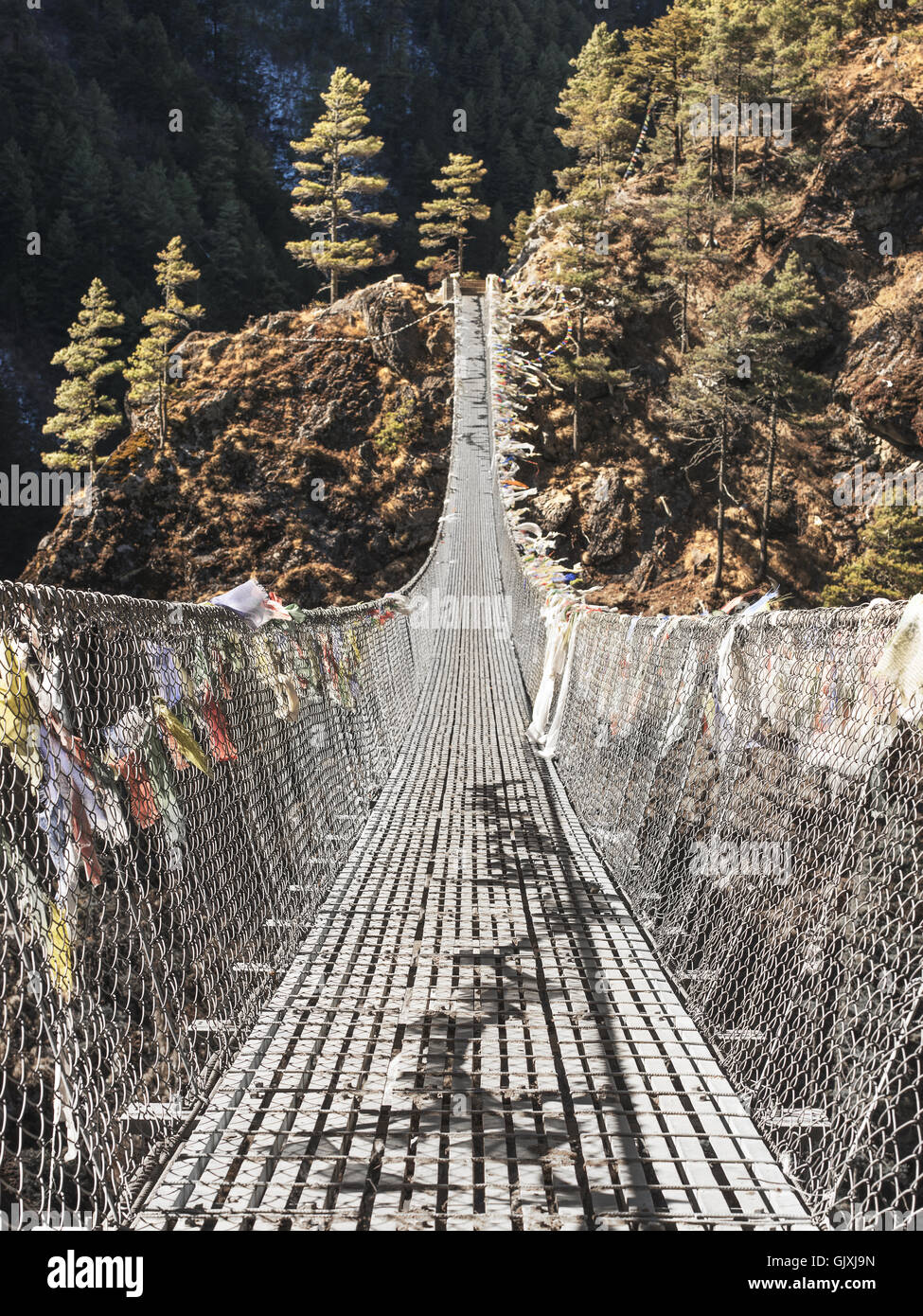 A suspended, prayer flag-covered bridge in the Himalayan Mountains of Nepal Stock Photo